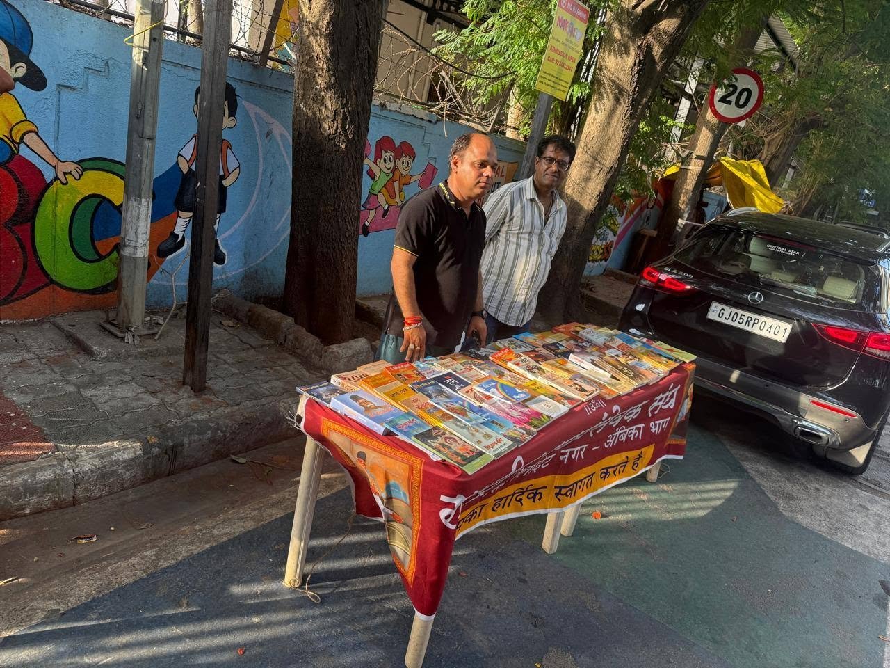Two volunteers standing beside a community book donation stall in Surat